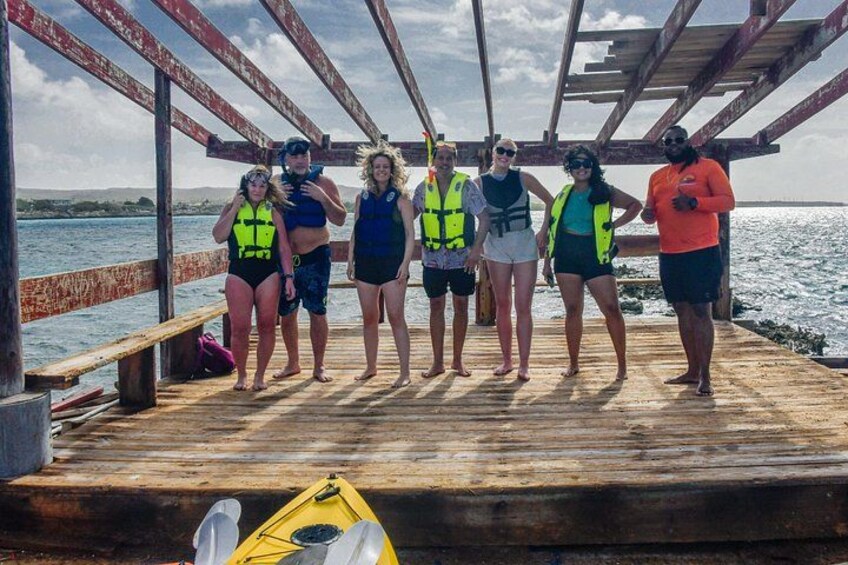 A group of people on a wooden dock by the water, wearing life jackets. 2
