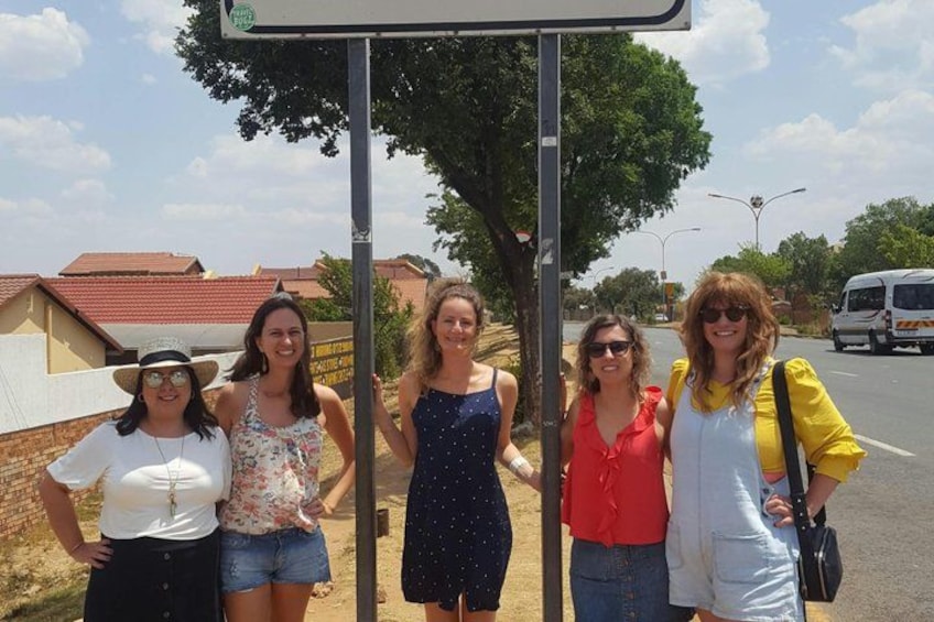 Un grupo de personas de pie junto a una señal de tráfico, con casas y una furgoneta al fondo. 4