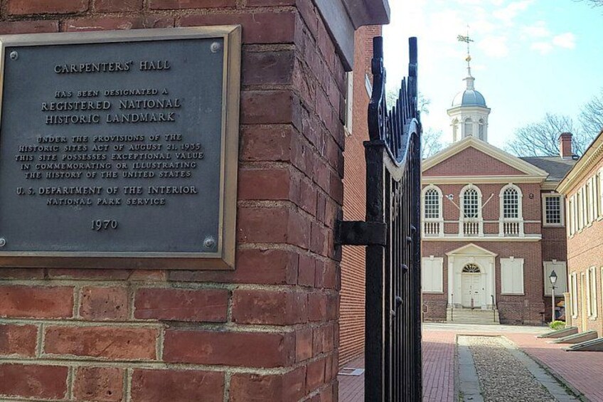 A brick building with a plaque, a gate, and a white building with a dome in the background. 2