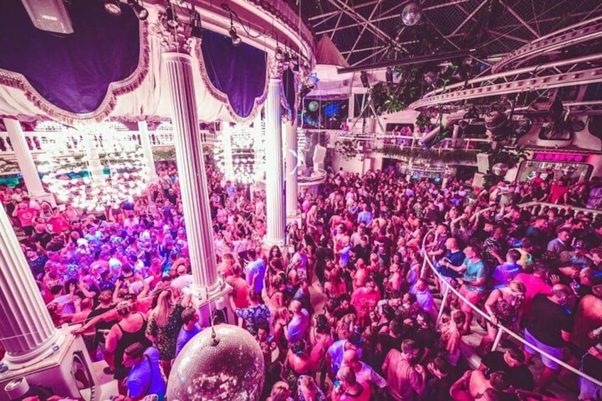 A crowded indoor venue with ornate columns and a disco ball. 4
