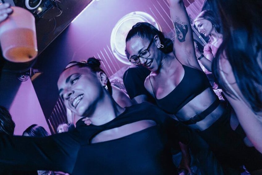 A group of people in a dimly lit room with purple lighting, some holding drinks. 5