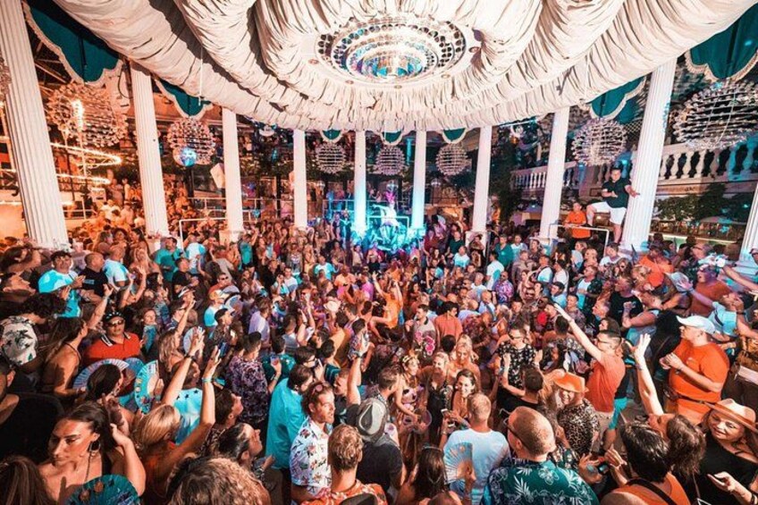 A crowded indoor event with a central stage, columns, and decorative ceiling elements. 5