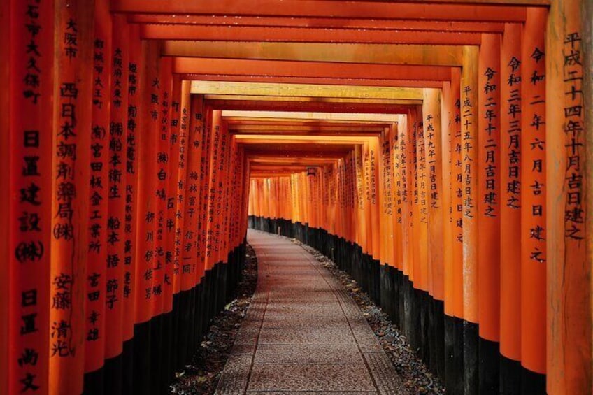 A corridor lined with orange torii gates with Japanese inscriptions. 1