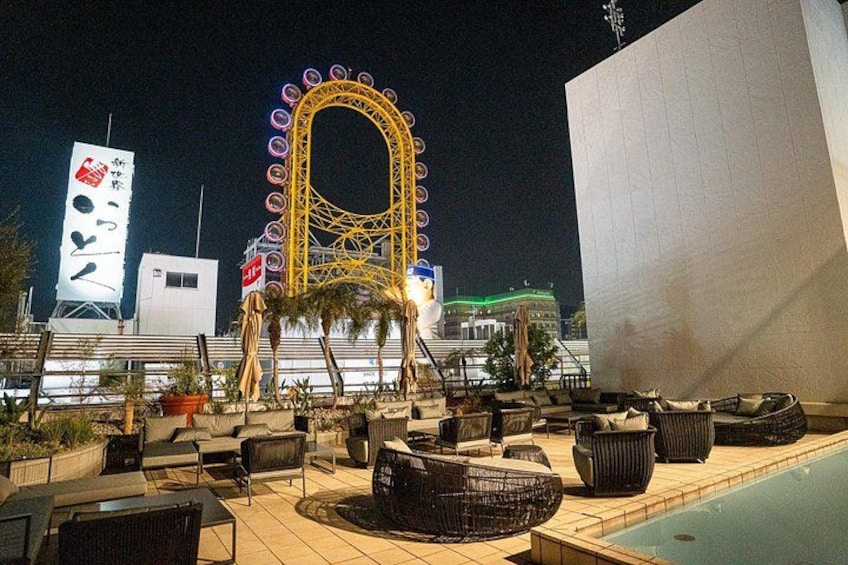 A rooftop bar with outdoor seating, a Ferris wheel in the background, and a pool. 2