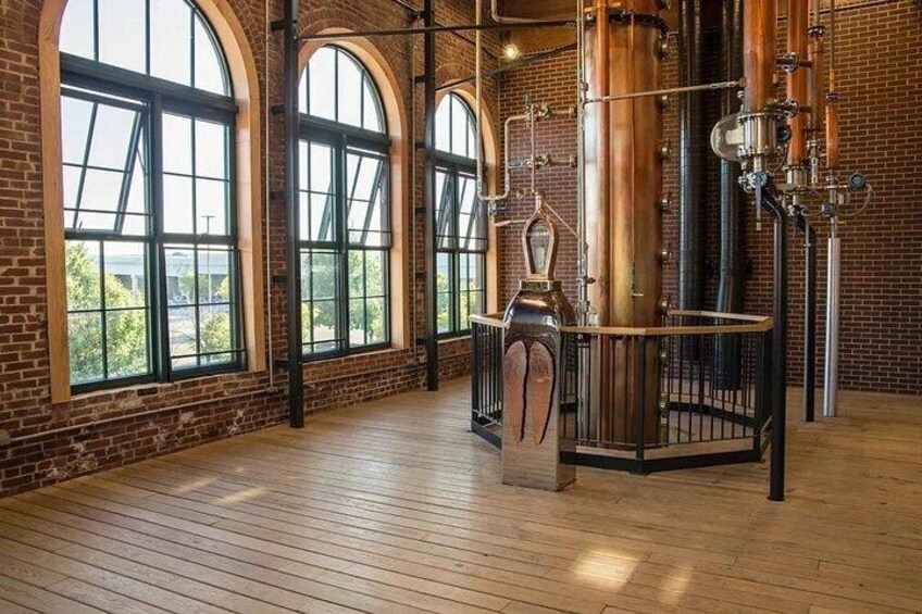 A spacious room with large arched windows, wooden flooring, and industrial brewing equipment. 3