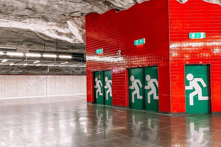 Une station de métro aux murs rouges, aux portes vertes indiquant les issues de secours et au sol poli. 2