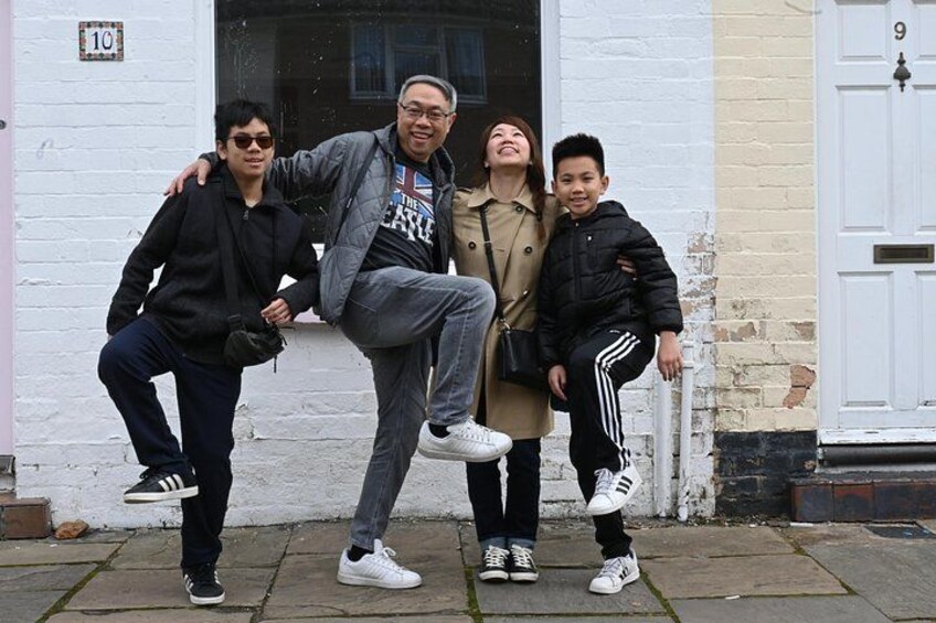Cuatro personas posando frente a un edificio blanco con una puerta negra y el número 9. 1