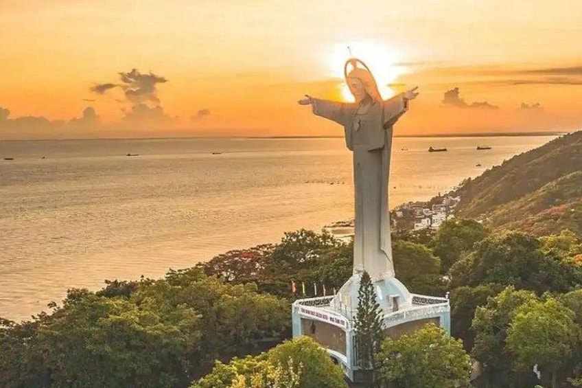 Een standbeeld met uitgestrekte armen, een kustlandschap en een zonsondergang. 2
