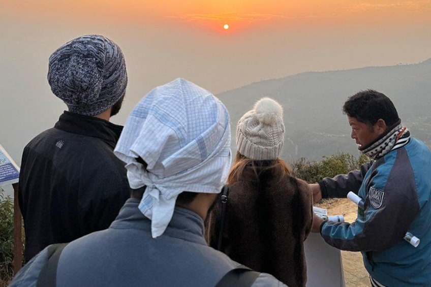A group of people standing on a hill overlooking a sunset. 5
