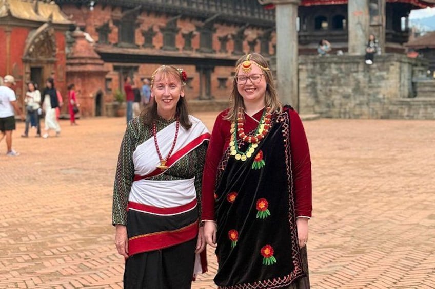 Two individuals in traditional attire standing in an outdoor setting with a historical building in the background. 3
