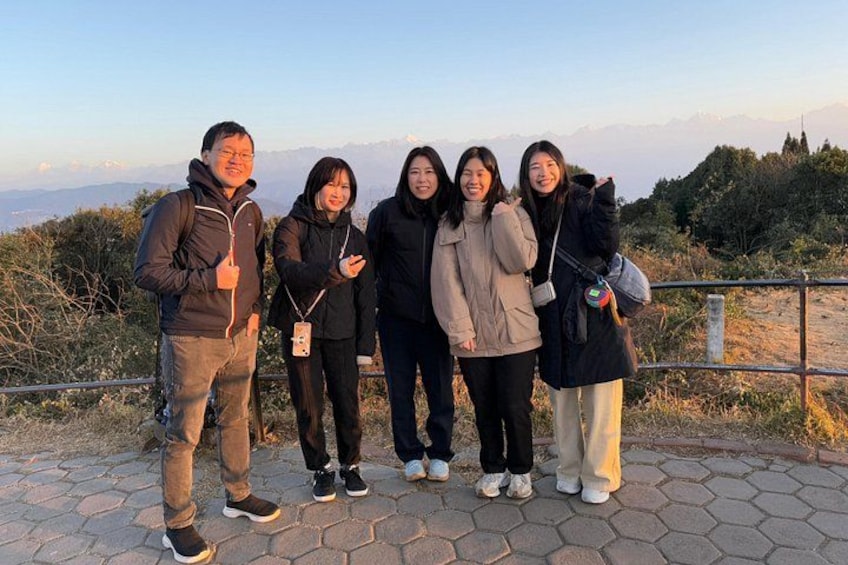 A group of people standing on a paved path with a mountainous landscape in the background. 1