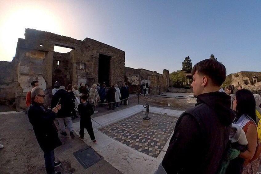 An ancient ruin with visitors, a mosaic floor, and stone walls. 2