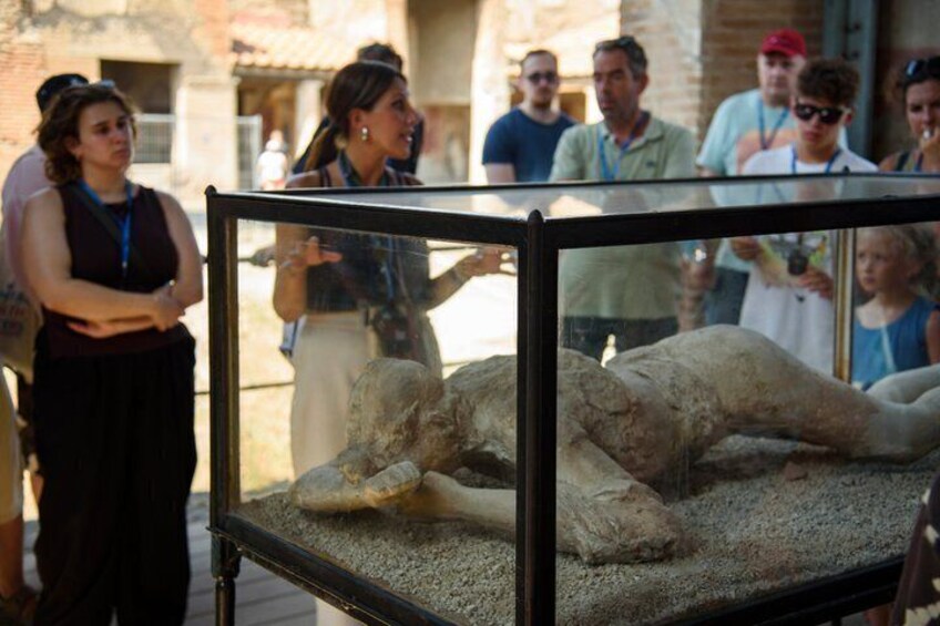 A mummy exhibit in a glass case with visitors observing it. 1