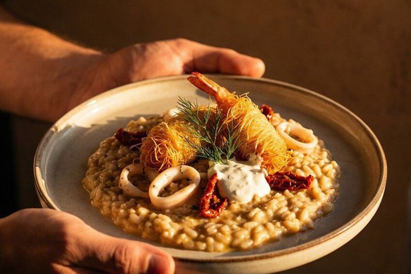 A plate of risotto with squid rings, a dollop of cream, and a garnish of dill and sun-dried tomatoes. 3