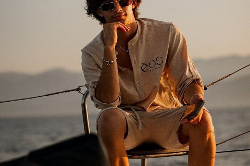 Iemand zit op een stoel aan het water, draagt een lichtkleurig shirt met een logo en houdt een hengel vast. 5