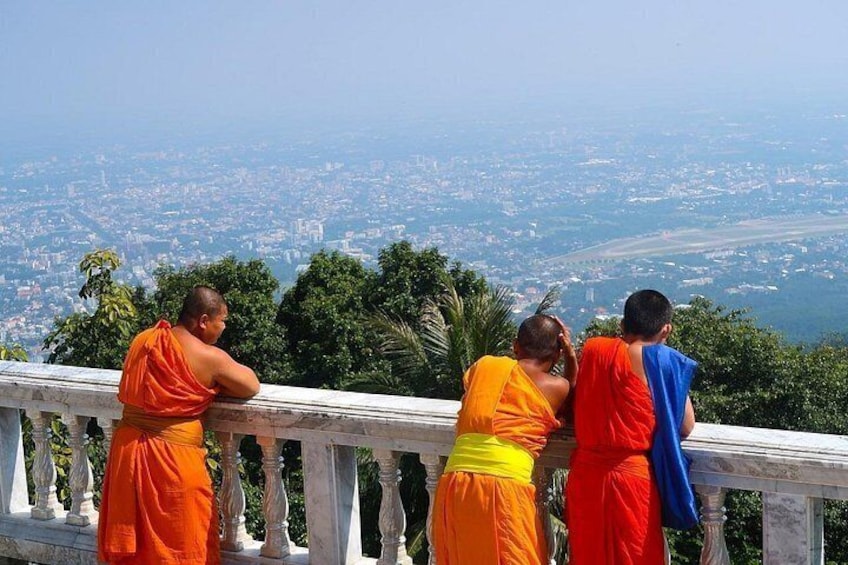 Monks in orange robes on a balcony overlooking a cityscape. 4