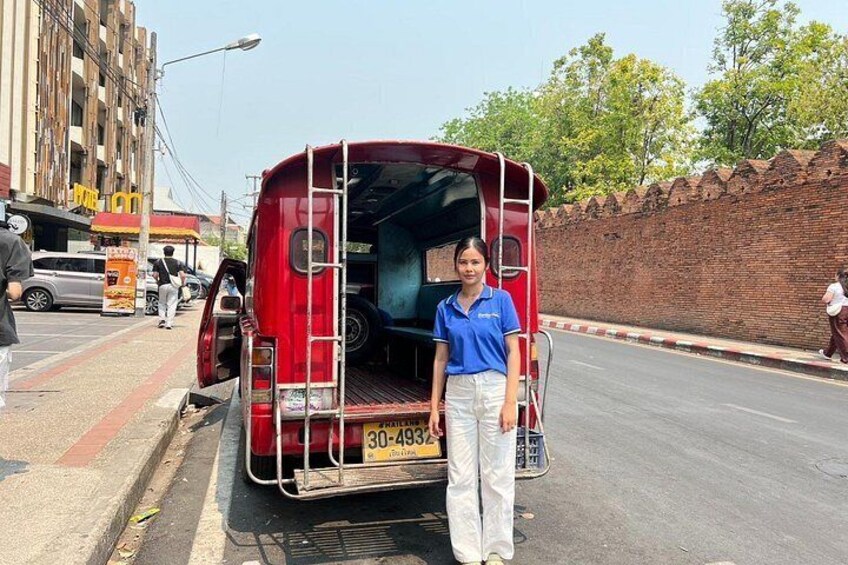 A red auto-rickshaw parked on a city street with a person standing next to it. 5