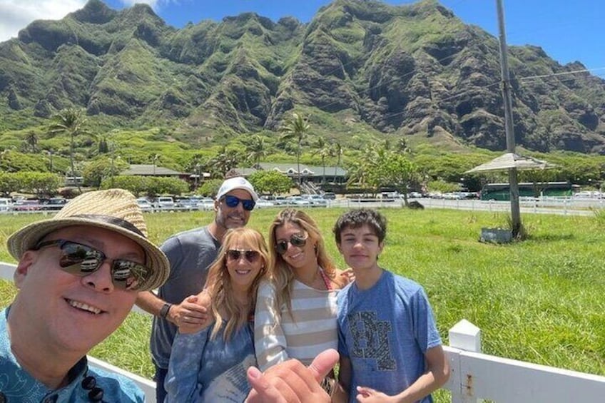 A group of people posing in front of a mountainous landscape with a road and parked cars in the background. 1