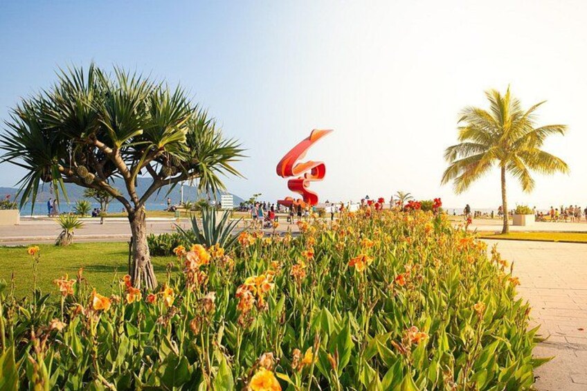 A landscaped area with a palm tree, a large red sculpture, and a flower bed. 4