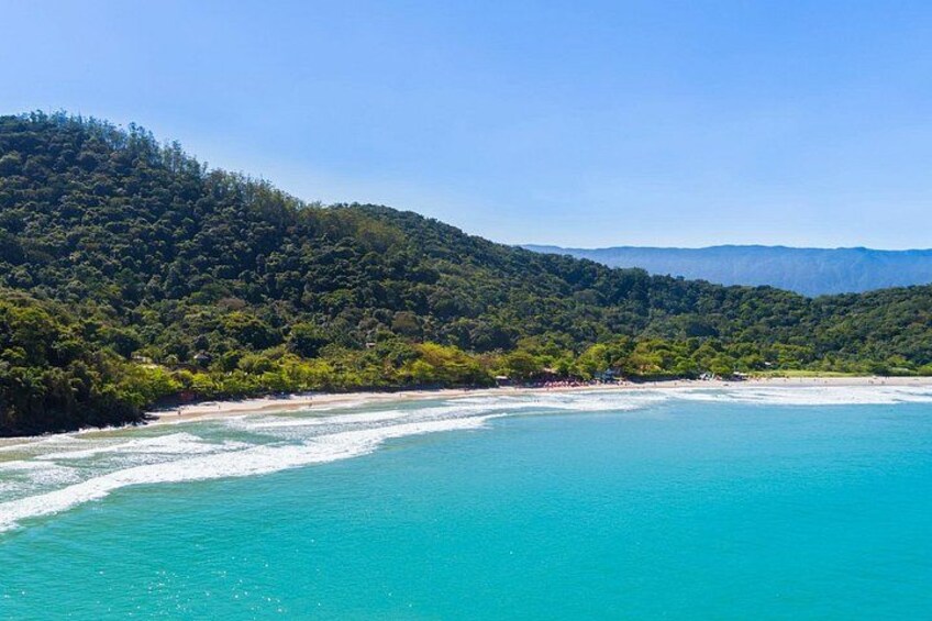 A coastal landscape with turquoise waters, a sandy beach, and a forested hill. 3