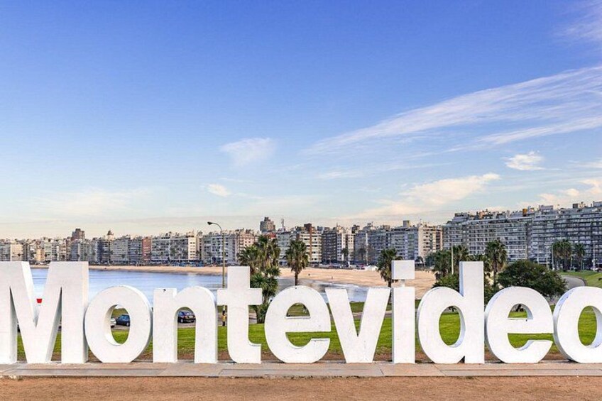 Stora, vita bokstäver som bildar ordet ”Montevideo” i en stadsbild med byggnader och en strand i bakgrunden. 4