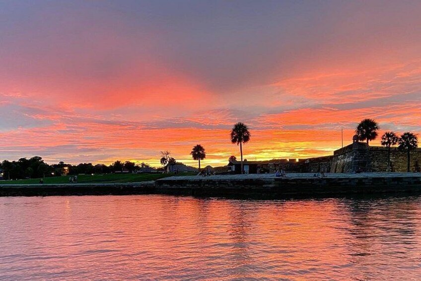 A sunset over a body of water with palm trees and a fort-like structure. 4