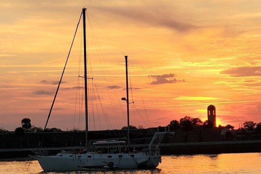 A sailboat on calm water during sunset with a tower in the background. 3