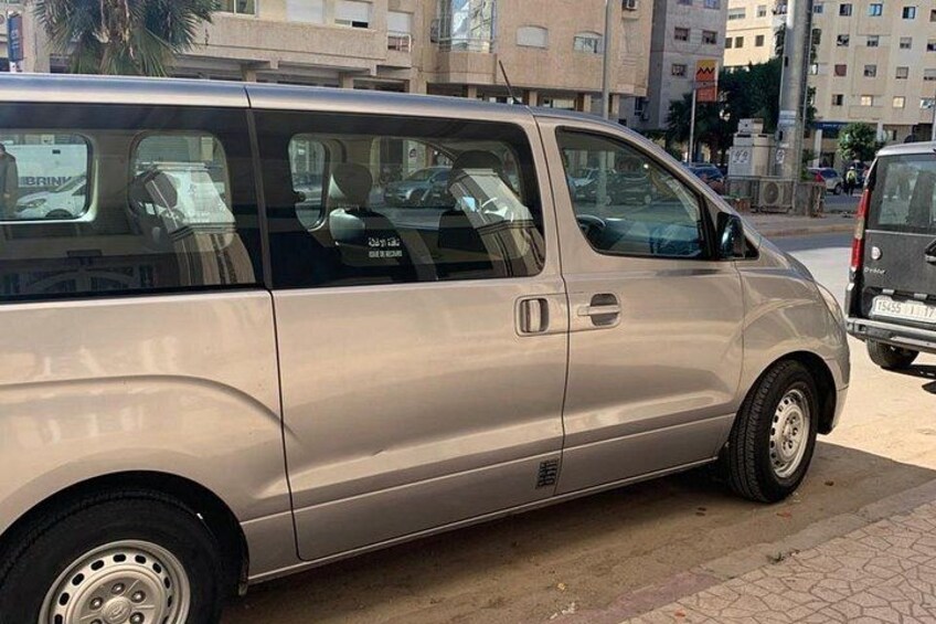A silver minivan parked on a city street with buildings in the background. 3