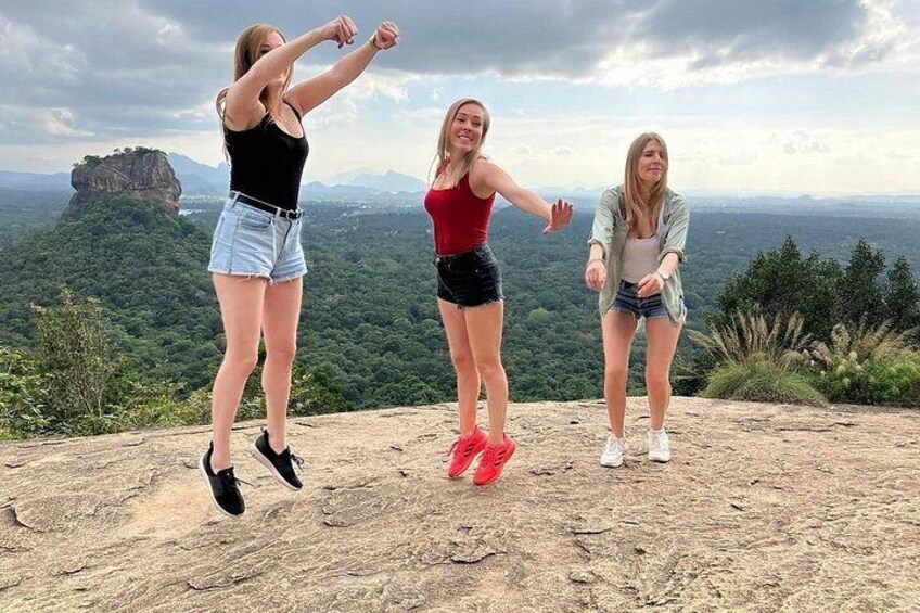 Three people jumping on a rocky outcrop with a mountainous landscape in the background. 1
