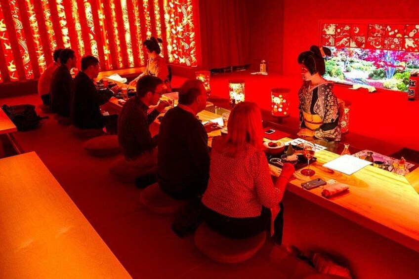 A group of people seated at tables in a dimly lit room with red ambient lighting. 2