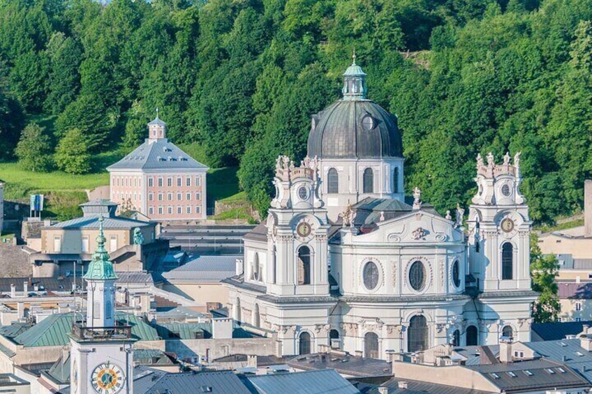 Una chiesa storica con una grande cupola e due torri, circondata da edifici urbani e una collina verde sullo sfondo. 3