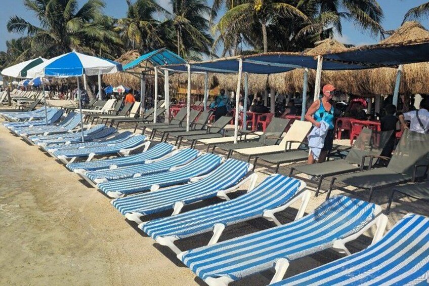 A beach with rows of striped lounge chairs and thatched umbrellas. 1