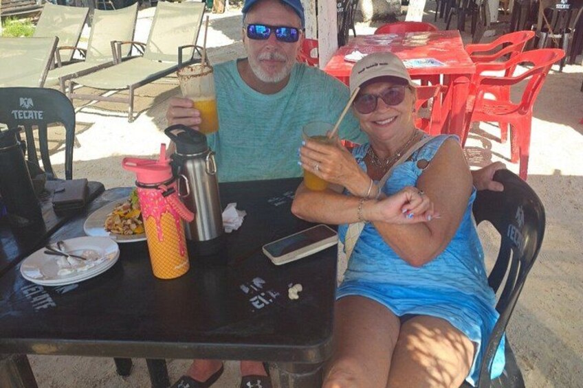 Two people sitting at an outdoor table with a meal and drinks. 2