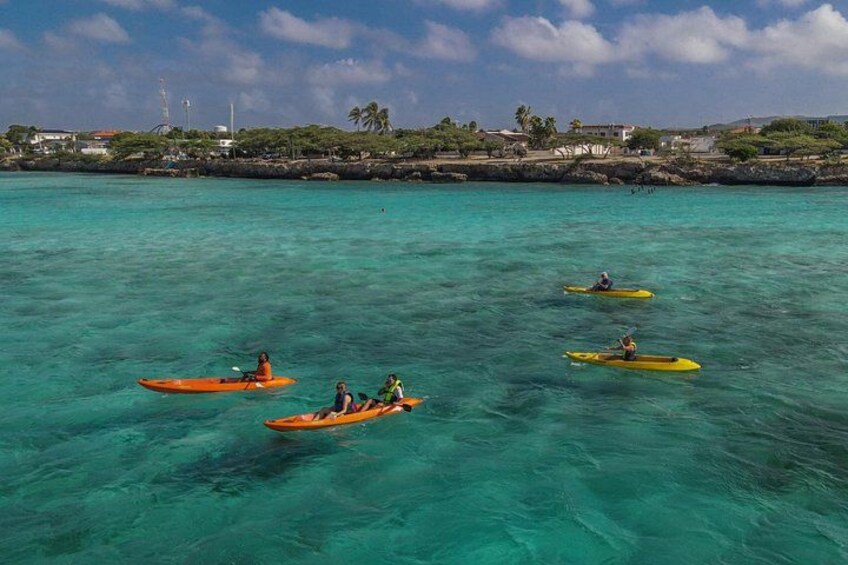 Kayakers on turquoise water with a coastal town in the background. 2