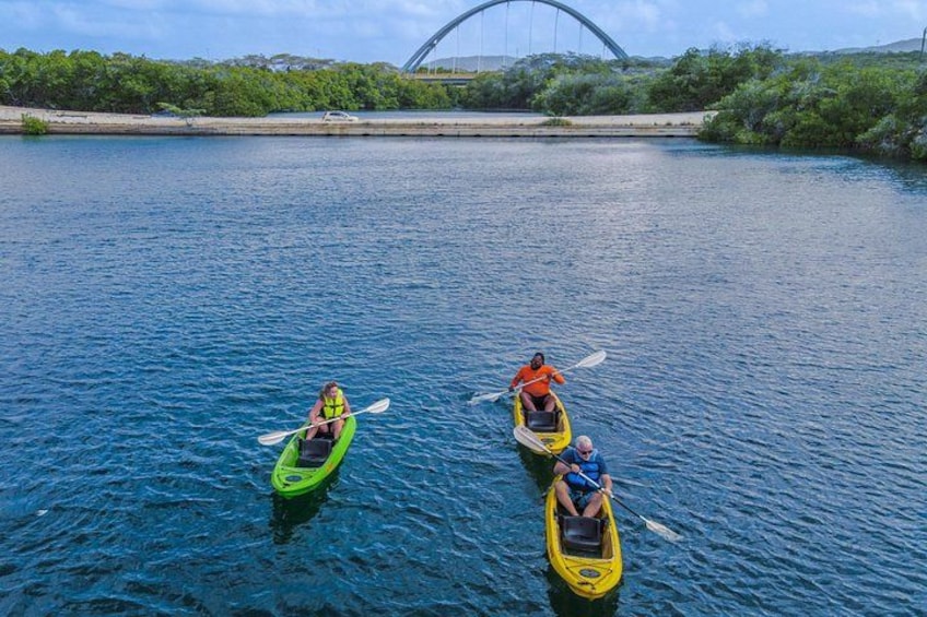 Three kayaks on a calm river with a bridge in the background. 3