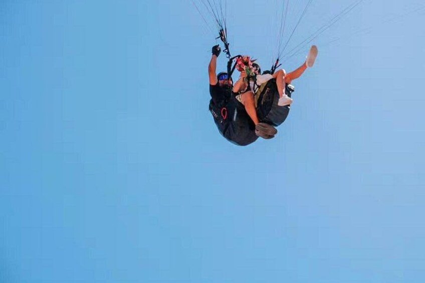 A person in a harness attached to a parachute, suspended in the air against a clear sky. 4