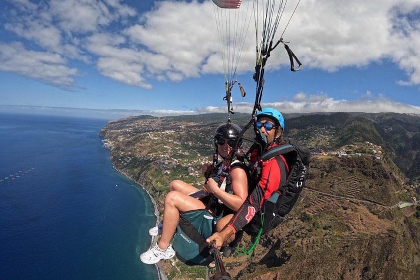 Two people paragliding over a coastal landscape with a view of the ocean and hills. 2