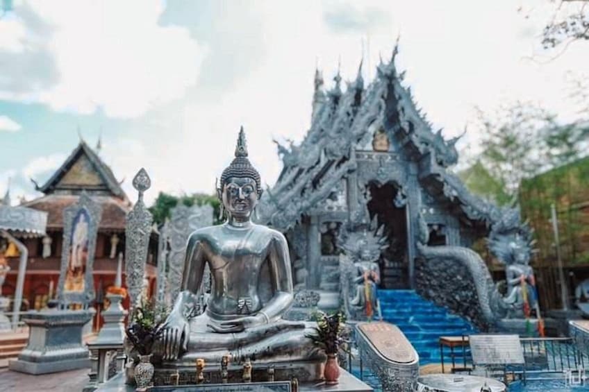 A large seated Buddha statue in front of a traditional Thai temple with ornate architecture. 2