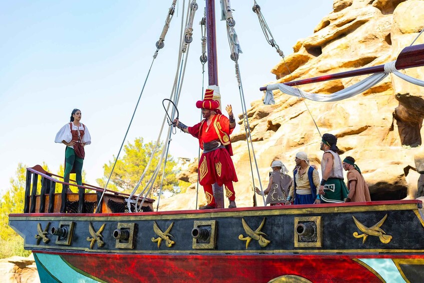 A pirate ship with a crew dressed in period costumes, anchored near rocky cliffs. 2