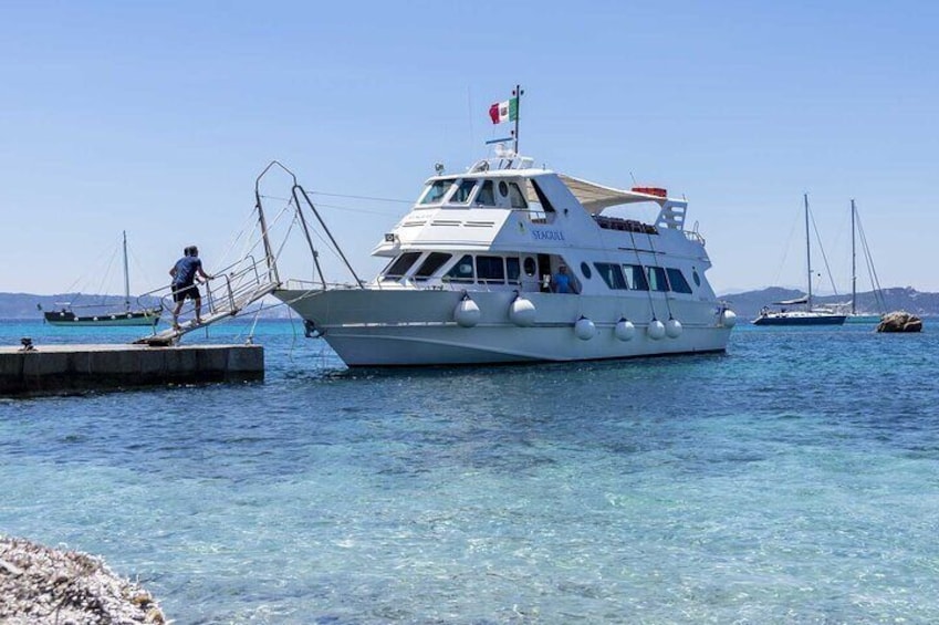 A white boat named 'SEACATELL' docked at a pier with clear blue water and a person boarding it. 1
