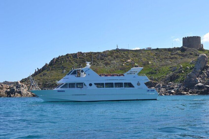A white yacht named 'SEAGULL' with the registration number 'LM 7840' sailing near a rocky coastline with a castle-like structure in the background. 3