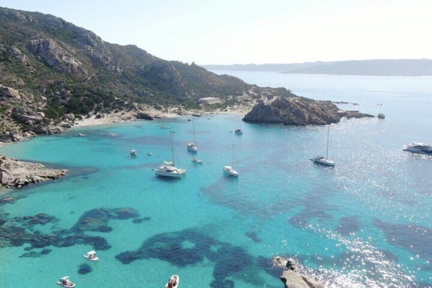 A coastal area with clear turquoise waters, boats anchored near rocky shores, and a hilly landscape in the background. 4