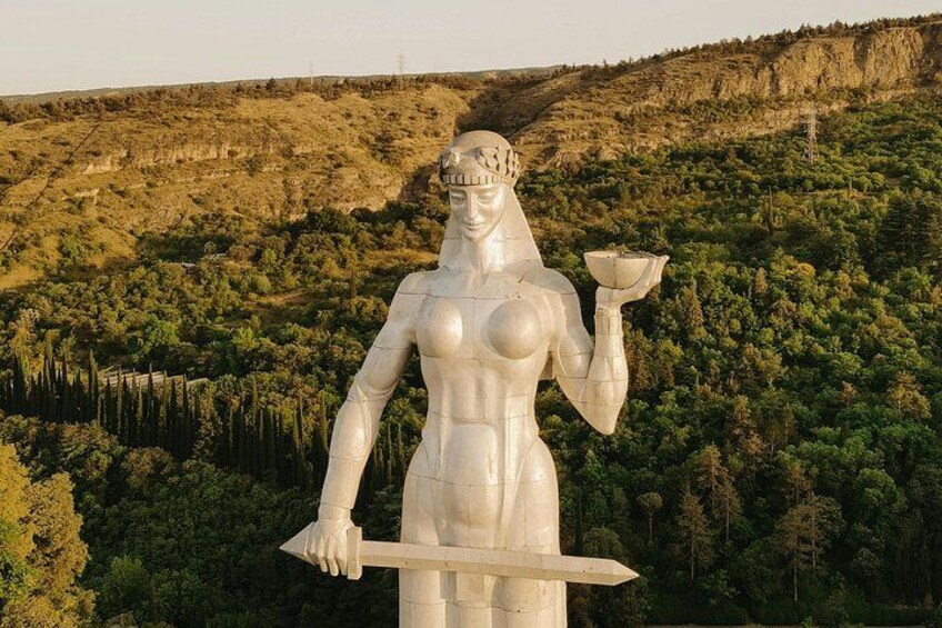 Una estatua grande de una mujer sosteniendo un cuenco y una lanza, frente a un paisaje montañoso. 3
