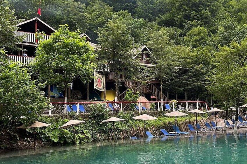A lakeside resort with wooden buildings, lounge chairs, and umbrellas. 2