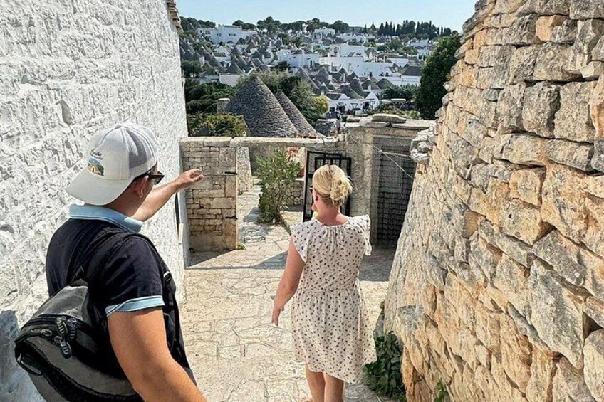 Un étroit sentier de pierre, bordé de touristes, un mur blanc et une vue sur une ville au loin. 2