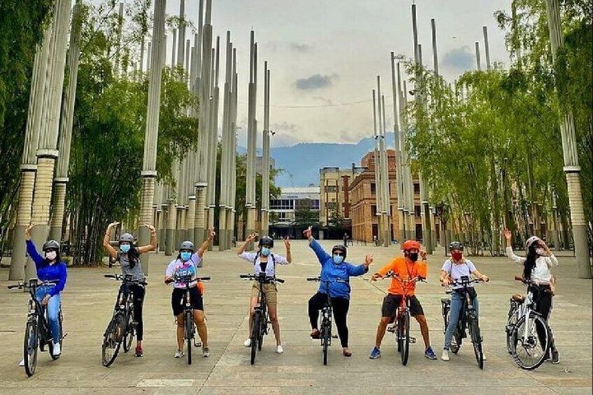 Eine Gruppe von Radfahrern auf einem Platz mit hohen, schlanken Säulen und Bäumen im Hintergrund. 3