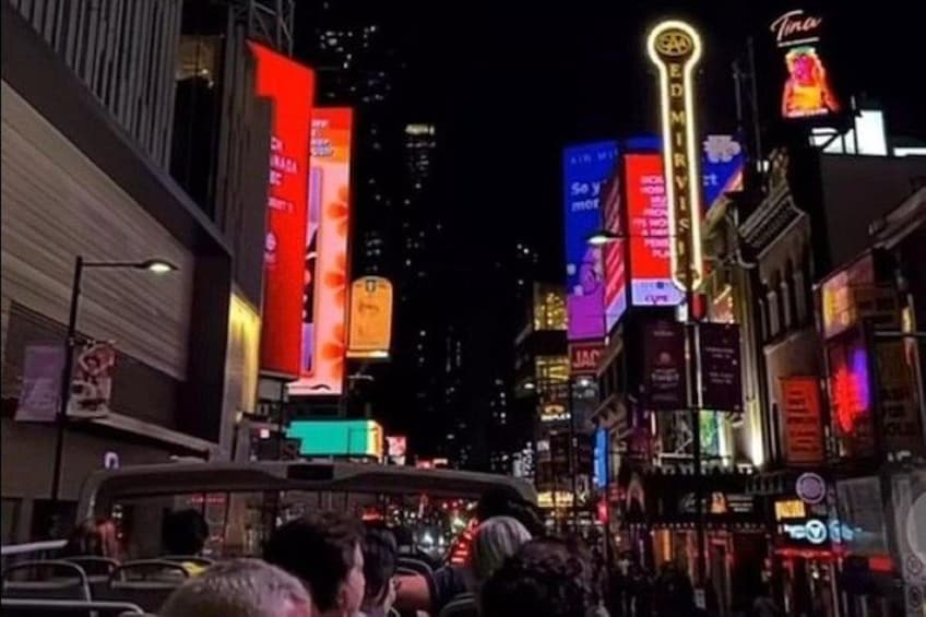Una concurrida calle urbana de noche, con vallas publicitarias y letreros de neón iluminados. 4