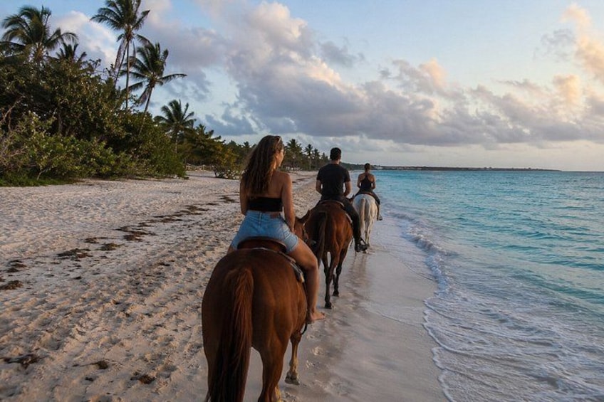 A beach with people riding horses along the shoreline. 1