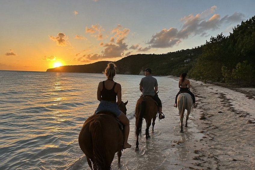 Three people horseback riding along a beach at sunset. 4