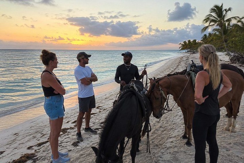 A group of people on a beach with horses and a sunset in the background. 2